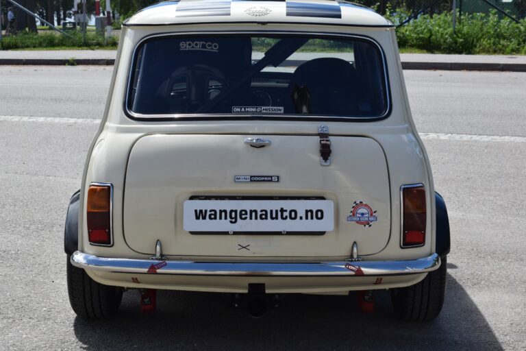 Rear view of a white vintage Mini Cooper S car with a roll cage, racing decals, and a license plate from Wangena Auto.