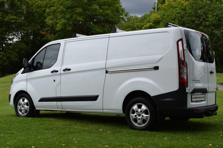 White cargo van with a sliding side door parked on a grassy area, surrounded by green trees under a cloudy sky.