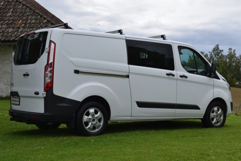 White cargo van parked on a grassy field near a country house with cloudy skies in the background.