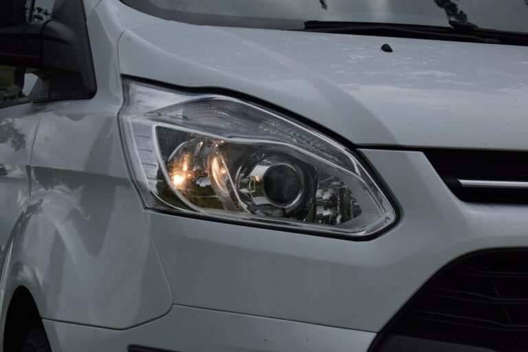 Close-up of the front headlight of a white van, showing a turned-on signal light and part of the grille.