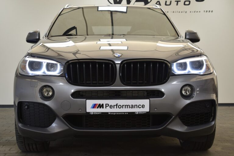 Front view of a grey BMW M Performance SUV displayed indoors, featuring illuminated headlights, a prominent grille, and an "M Performance" license plate on the bumper.