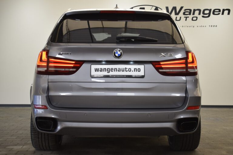 A rear view of a gray BMW X5 parked indoors at Wangen Auto dealership. The car's tail lights are on, and the license plate reads "wangenauto.no".