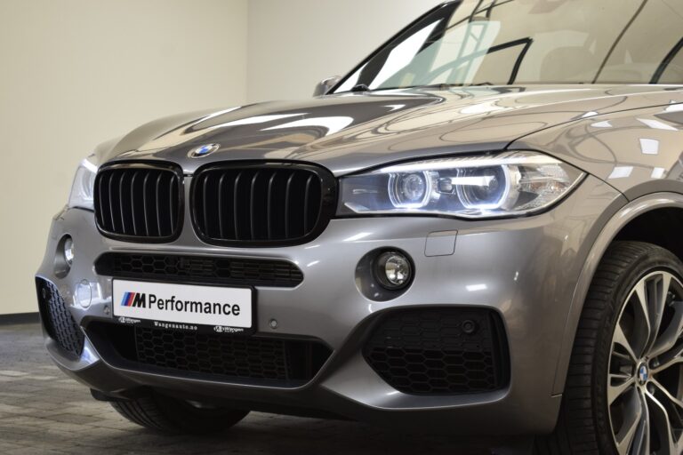 Close-up of a gray BMW SUV front, highlighting its headlights, grille, and M Performance badge.