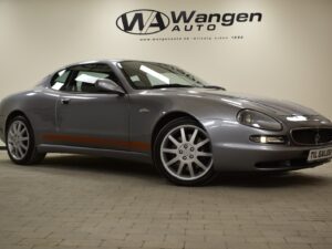 A silver Maserati sports car is displayed in a showroom with a "Wangen Auto" sign on the wall. The front license plate reads "TIL SALGS.