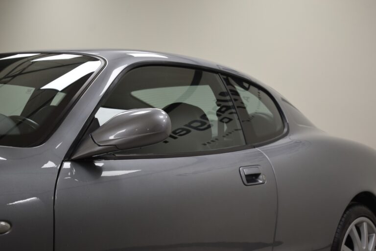 Side view of a grey sports car showcasing the driver's side window, side mirror, and door handle against a plain background.