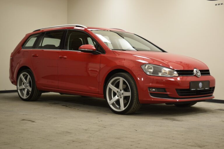 A red Volkswagen Golf wagon is parked indoors on a grey tiled floor, slightly turned to the right. The car features silver alloy wheels and roof rails, with a clean and modern design.