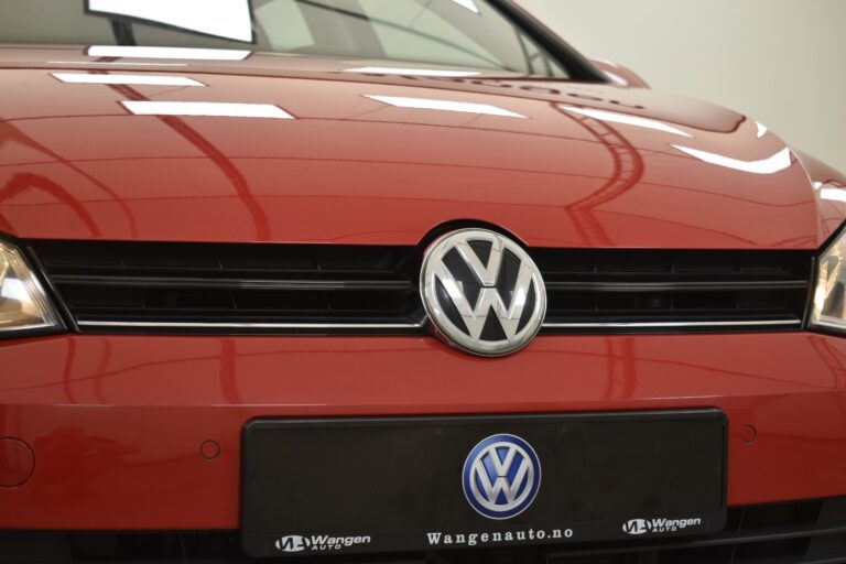 Close-up of the front grille of a red Volkswagen car, displaying the Volkswagen logo and a license plate with the text "Wangenauto.no.