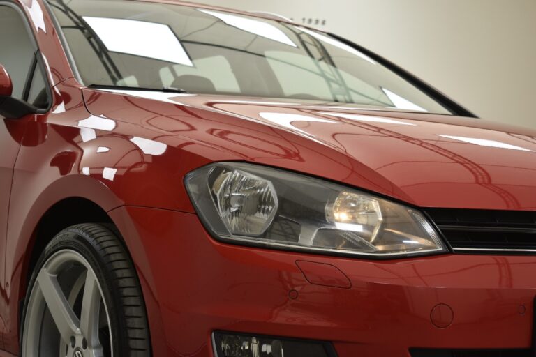 Close-up of the front end of a red car, showing the headlight, part of the grille, and the front wheel.