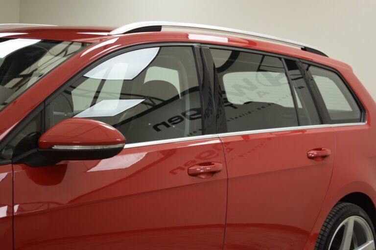 Close-up of the side view of a red car, focusing on the rear door, side mirror, and window, displaying the vehicle's sleek design and reflective surface.