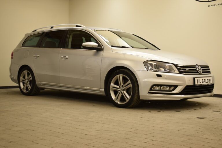 A silver Volkswagen station wagon is parked indoors on a tiled floor, with a "Til Salgs!" sign in the front indicating it is for sale.