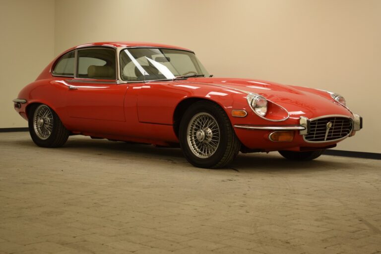 A red classic car with chrome details parked indoors on a beige tiled floor.