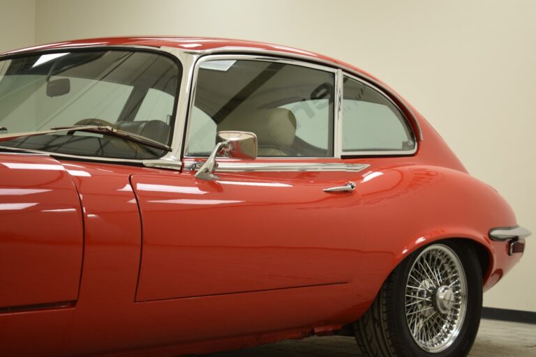 A side view of a red vintage car with chrome detailing and wire-spoke wheels parked indoors.