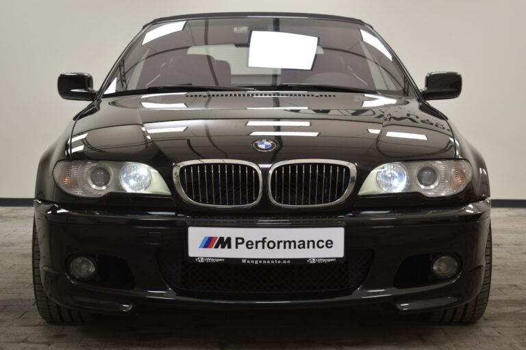 Front view of a black BMW car with illuminated headlights and an "M Performance" license plate.