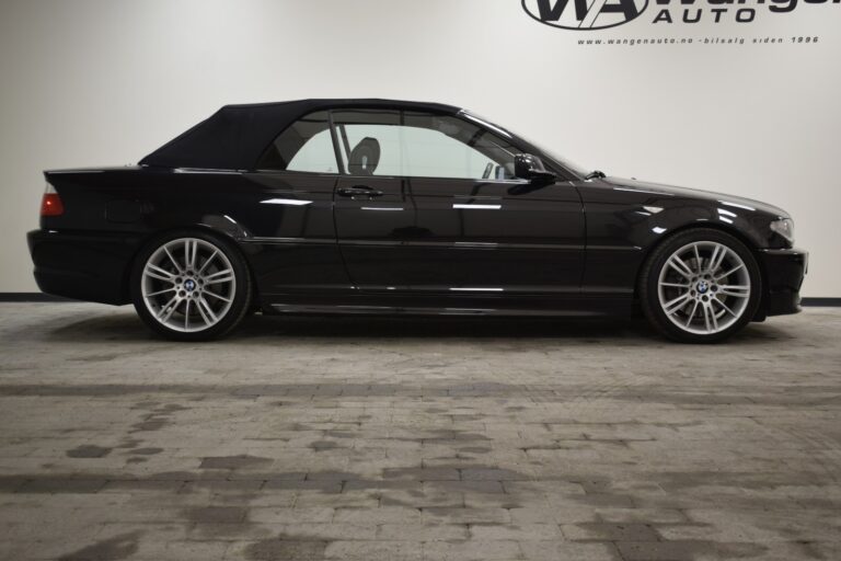 A black convertible car with a soft top roof and silver alloy wheels is parked on a brick floor against a plain wall with a logo that reads "Wagen auto".