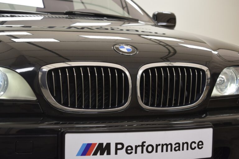 Close-up of a black BMW car’s front grille with the logo visible, and an "M Performance" license plate.