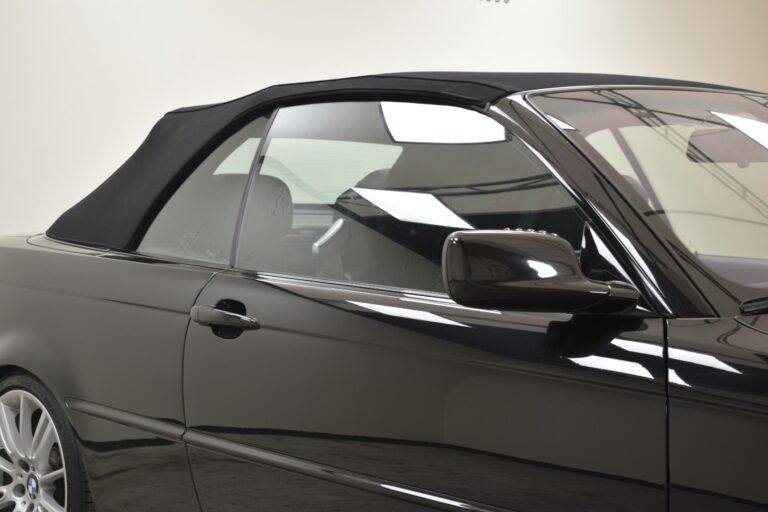 Close-up of a black convertible car with the top up. The car is shown from the side, focusing on the door, window, and rearview mirror.