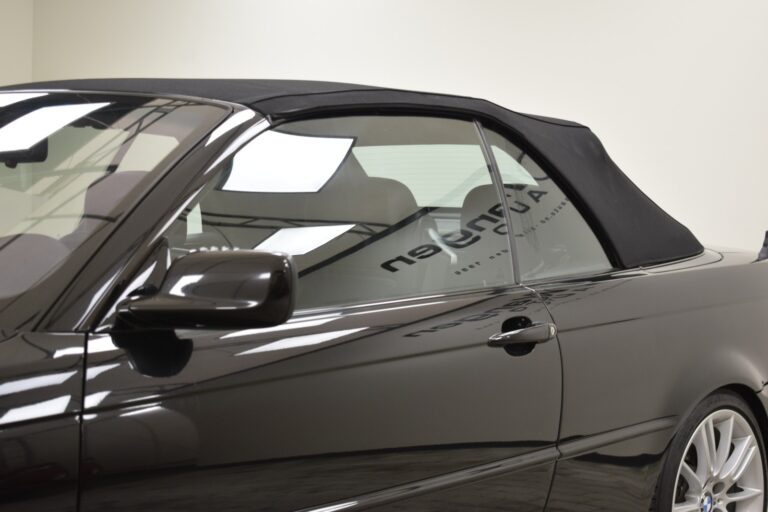 A black convertible car with its top closed, parked in an indoor setting with reflections of the ceiling lights visible on its glossy surface.