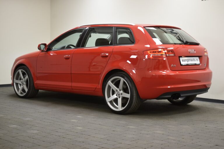 A red Audi hatchback is parked indoors on a tiled floor. The car has five doors and alloy wheels.