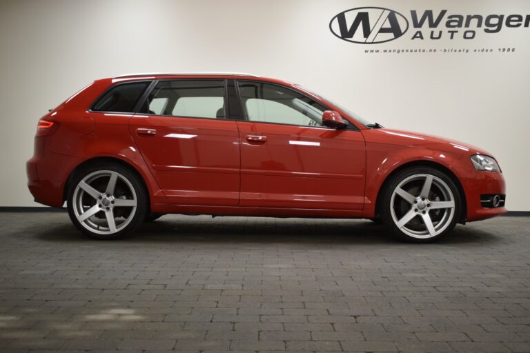 A red Audi SUV is parked indoors on a gray brick floor, with the logo and name "Wanger Auto" displayed on the wall behind it.