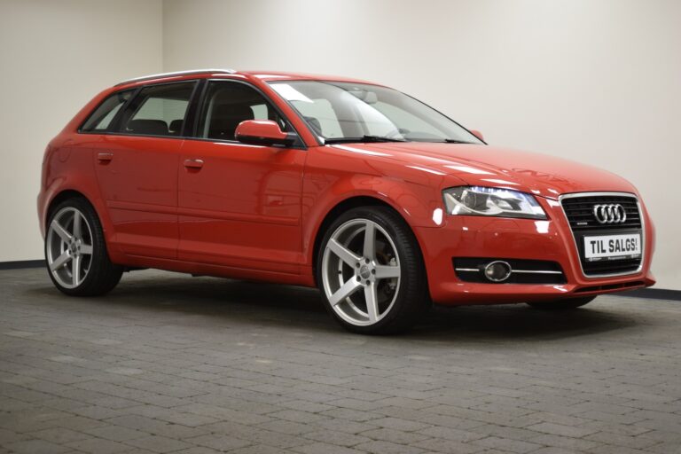 A red Audi hatchback with silver alloy wheels is parked in a room with gray tiled flooring. A sale sign is visible on the front of the car.