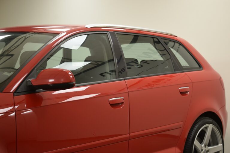 A close-up of the side of a red car, focusing on the driver's side door and rear passenger door against a neutral background.