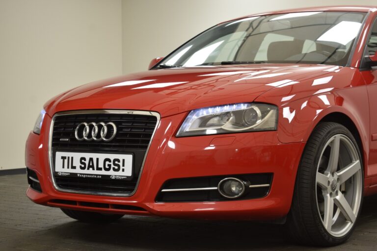 A red Audi car with a "Til Salgs!" (For Sale!) sign on the front license plate, displayed indoors.