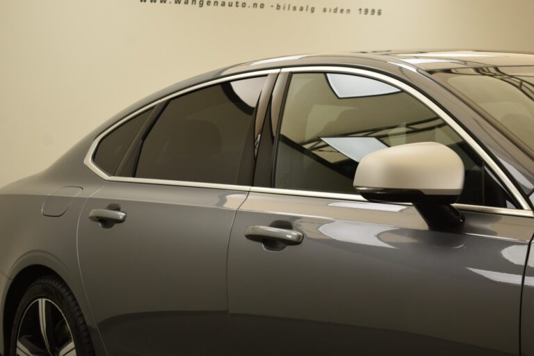 A close-up of the driver's side and rear passenger door of a silver sedan with tinted windows and a side mirror. A website URL is seen in the background.