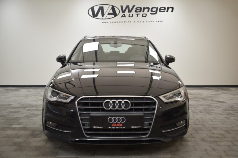 Front view of a black Audi car parked in a showroom with the Wangen Auto logo displayed on the wall behind it.