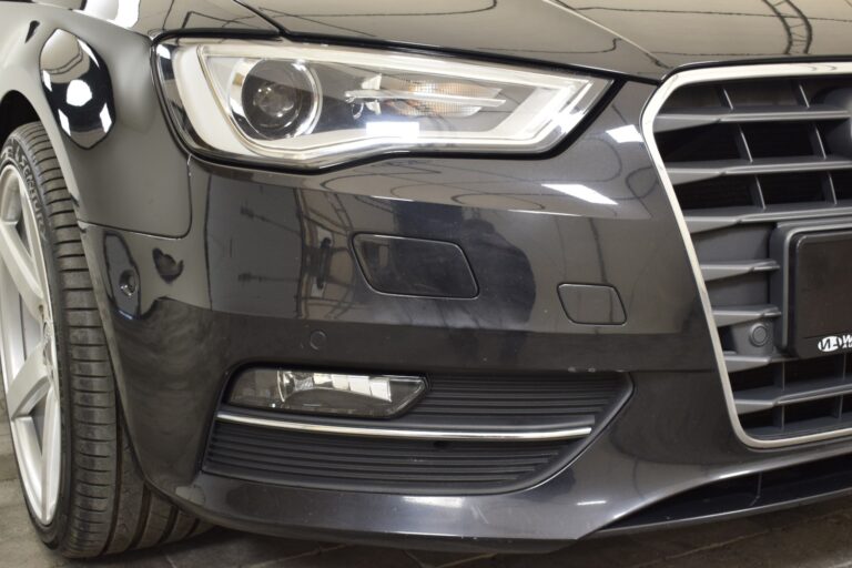 Close-up of the front left side of a black car showing the headlight, grille, and part of the bumper.