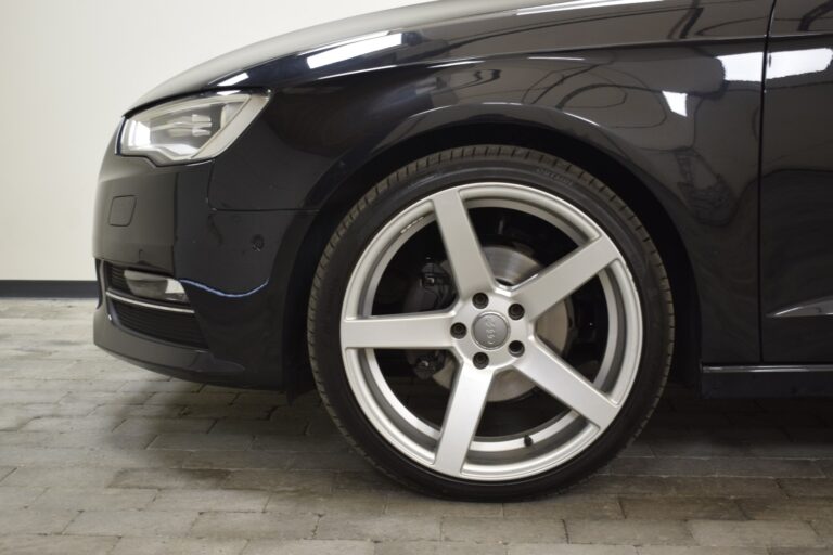 Close-up view of the front left wheel of a black car, featuring a silver alloy rim and low-profile tire on a paved surface.