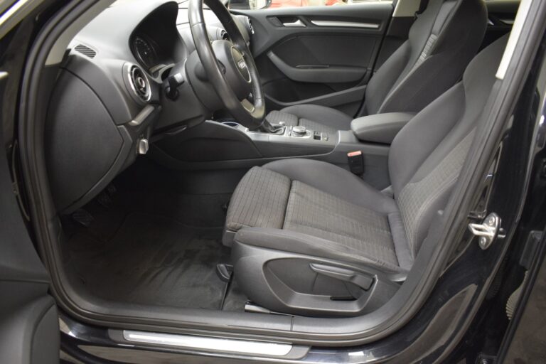 Interior view of a car showing the front seats, steering wheel, dashboard, and center console, all in black upholstery and materials.