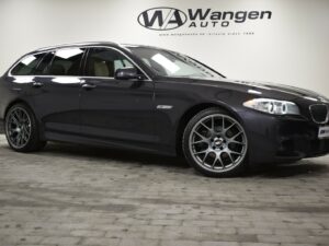 A black BMW station wagon parked indoors on a concrete floor, with Wangen Auto's logo displayed on the wall in the background.