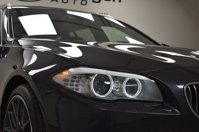 Close-up of a car's front end showcasing sleek design and headlight detail, with reflections on the glossy surface.