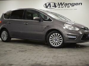 A gray minivan displayed indoors at a showroom, with a Wangen Auto sign in the background.