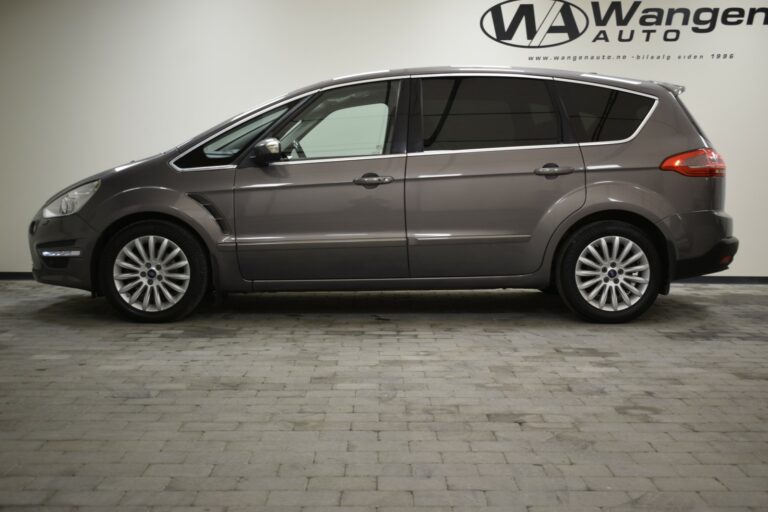 A gray minivan is parked indoors on a tiled floor, with a visible logo on the wall in the background.