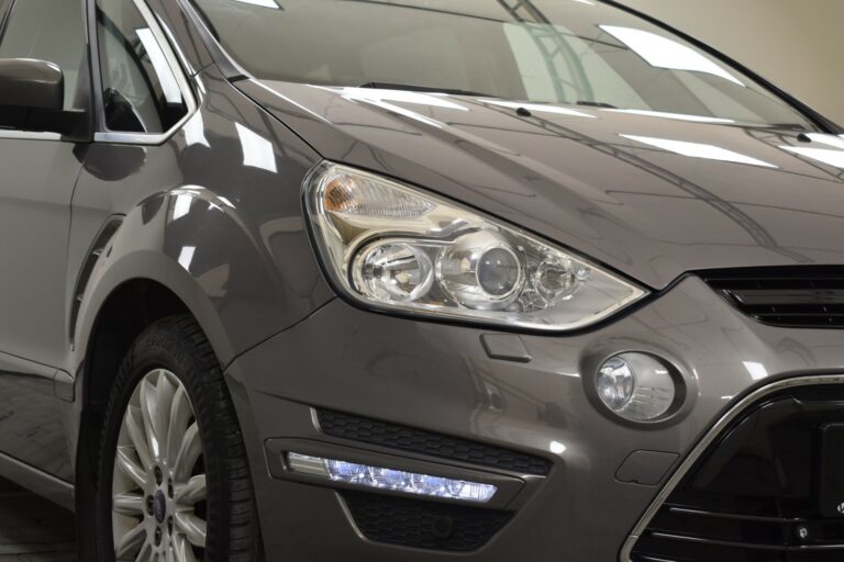 Close-up of the front left side of a gray car, showing the headlight, side mirror, and part of the grille.