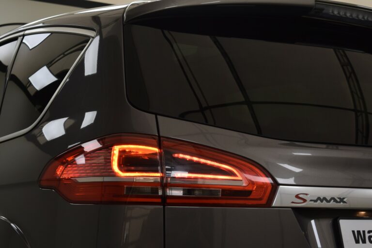 Close-up of the rear left taillight of a gray S-Max vehicle, showing illuminated red lights and part of the vehicle's rear window.