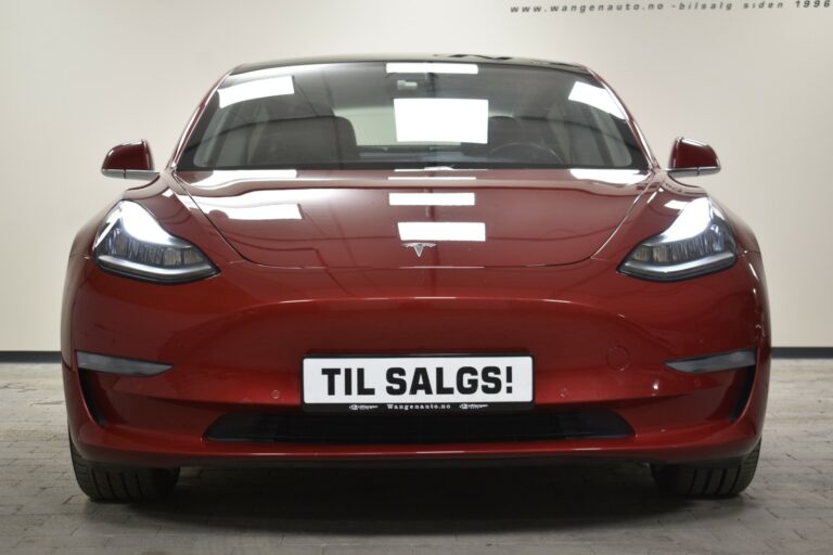 A red Tesla car with headlights on, displaying a "TIL SALGS!" sign on the front bumper.