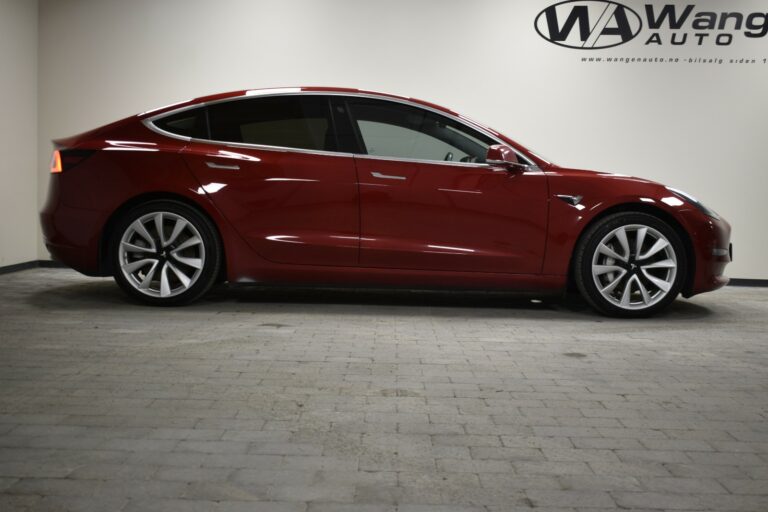 A red electric sedan is parked indoors, viewed from the side.