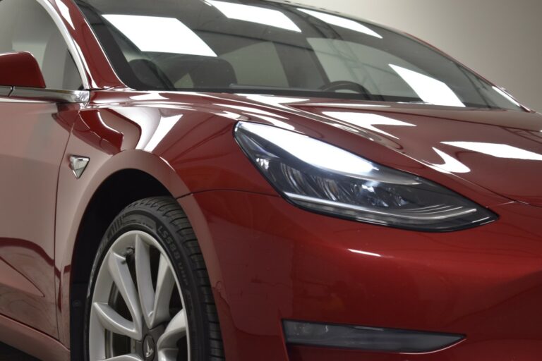 Close-up of a red electric car's front, showing its headlight and part of the wheel.