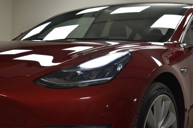 Close-up of a red car's front section, highlighting a sleek headlight design and smooth body lines.