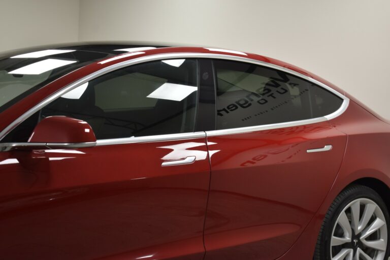 Side view of a shiny red car parked indoors, featuring a sleek design with tinted windows and chrome trim.