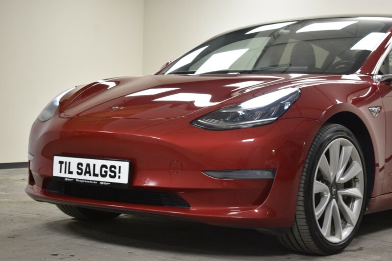 Red Tesla car with a "Til Salgs!" sign on the front, indicating it is for sale, parked indoors.