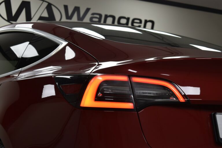 Close-up of a red car's rear left taillight with illuminated LED lights, parked indoors.