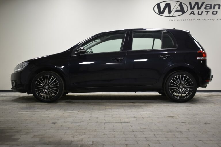 Side view of a black hatchback car with alloy wheels parked indoors against a light wall.