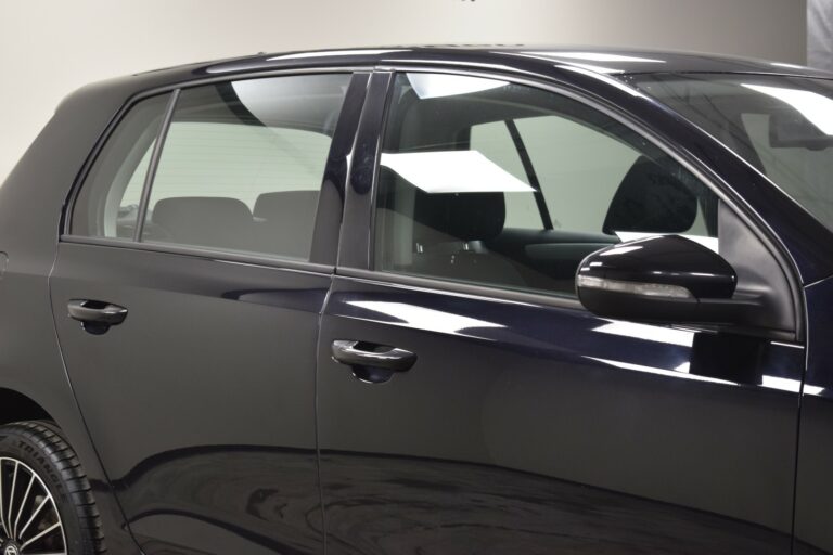 Close-up of the side of a black car showing the rear door and side mirror. The windows are closed and the car is indoors.