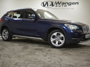 A blue BMW SUV parked indoors with a Wangen Auto logo on the wall behind it.