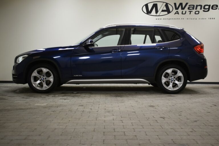 A blue SUV parked indoors on a gray tiled floor, with a company logo on the wall in the background.