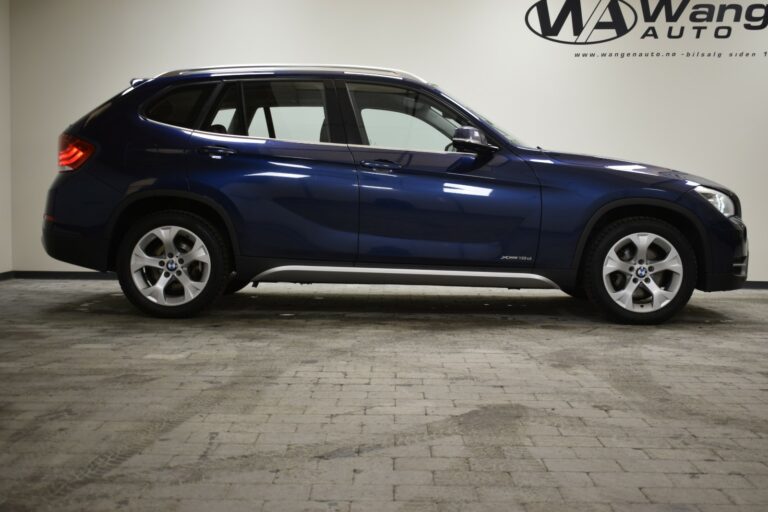 Side view of a blue SUV parked indoors on a tiled floor, with a logo visible on the wall in the background.