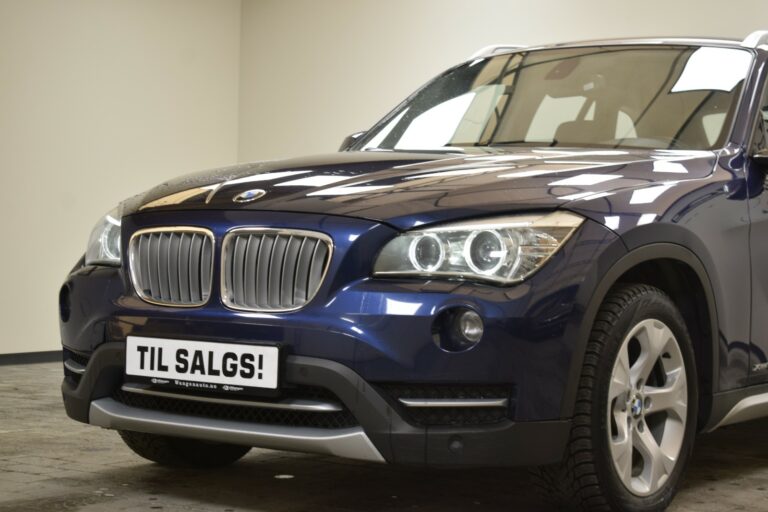 Close-up of a parked blue BMW SUV in a garage with a sign on the front reading "TIL SALGS!" indicating it is for sale.